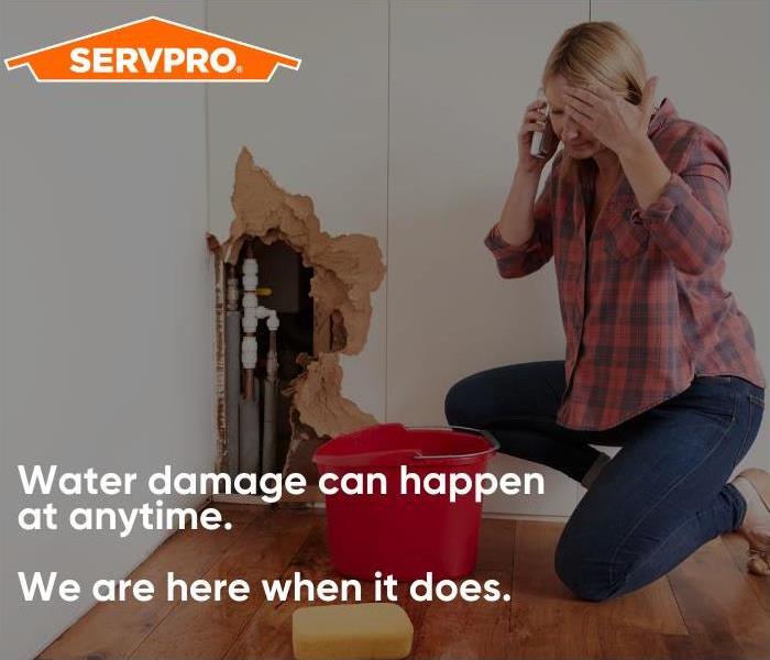 Women on the phone with a torn up wall and pipes exposed in the background.  SERVPRO logo and text